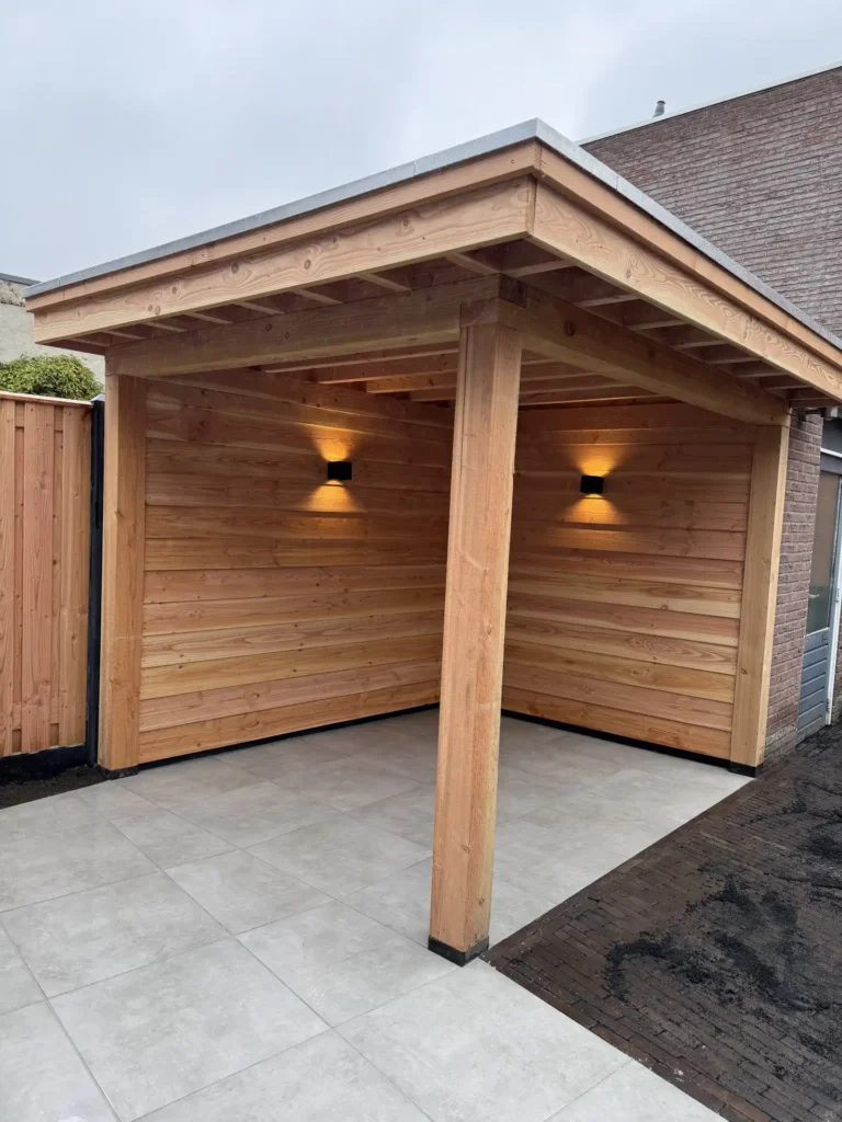 Houten overkapping met plat dak en zwarte wandlampen met sfeerverlichting bij een bakstenen gevel