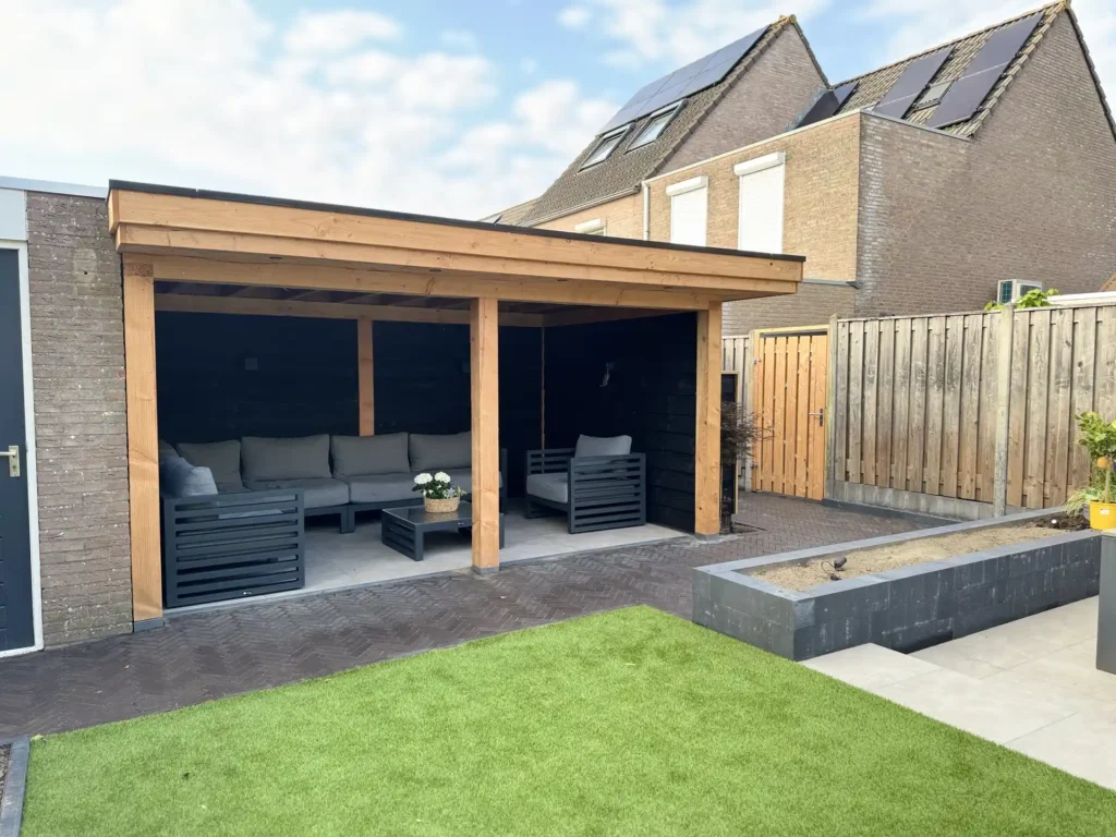 Houten overkapping met loungeset in een achtertuin met kunstgras, klinkerbestrating en antraciet plantvak