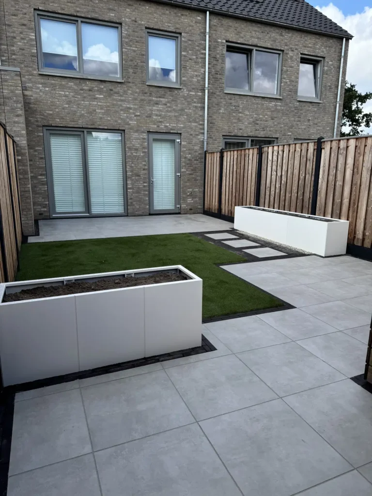Terras met bestrating, houten schutting en witte plantenbak achter een moderne woning met bakstenen gevel