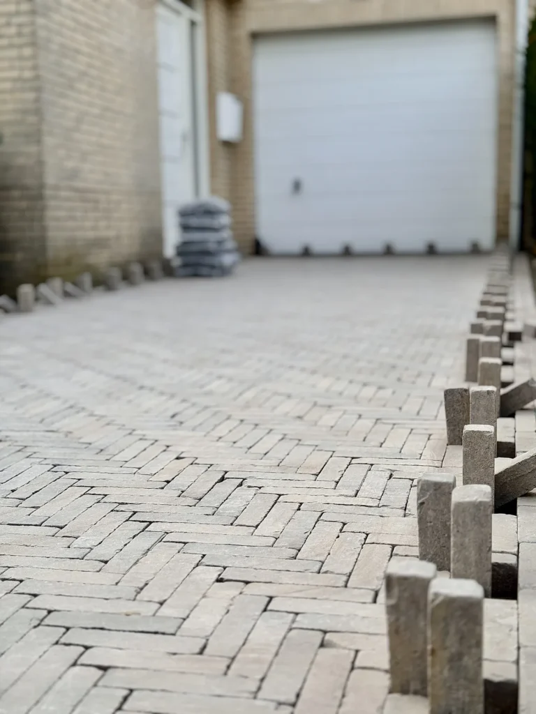 Oprit met grijze klinkerbestrating in aanleg bij een garage met stapels klinkers