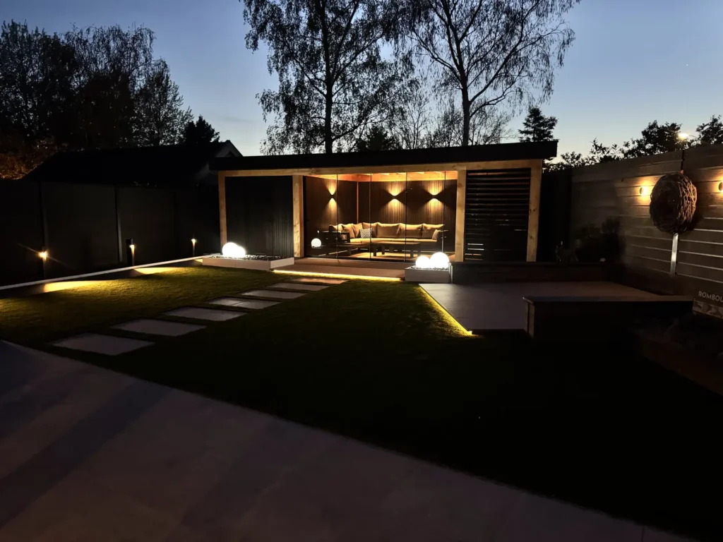 Moderne tuin in de avond met sfeervolle tuinverlichting, verlichte stapstenen, overkapping en loungeset