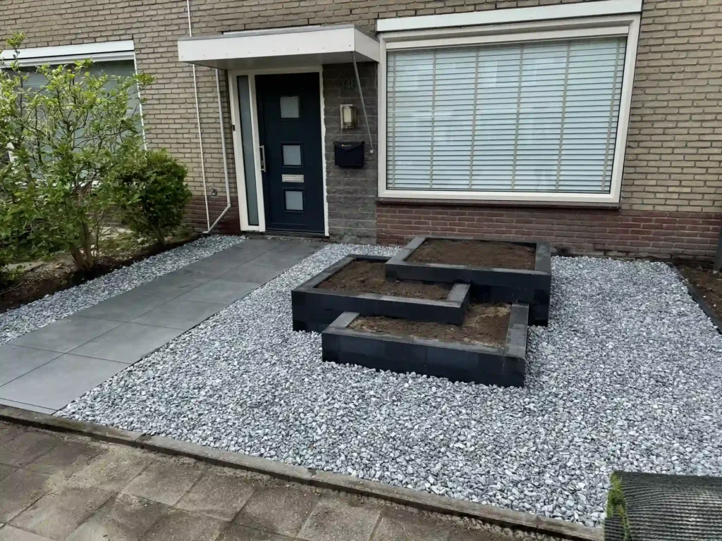 Onderhoudsvriendelijke voortuin met siergrind, antraciet plantvakken en een grijs tegelpad naar de voordeur