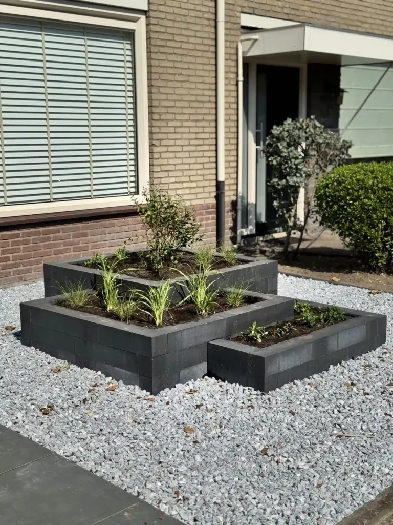 Voortuin met verhoogd plantvak en beplanting bij de entree van een woning met bakstenen gevel