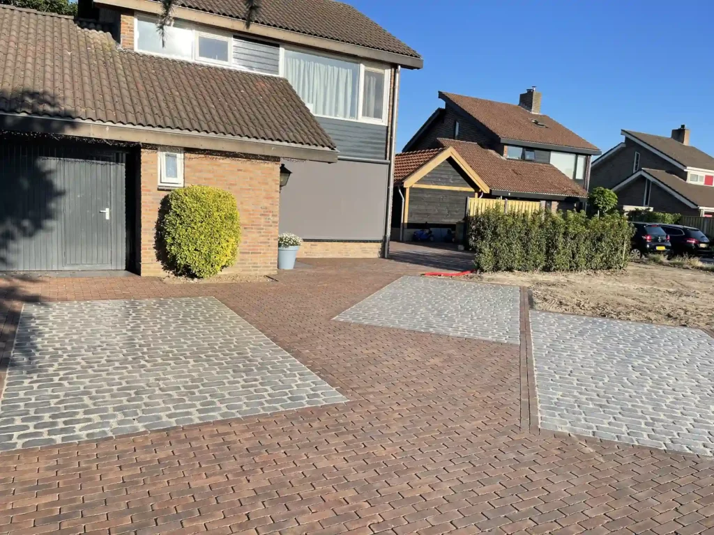 Ruime oprit en voortuin bestraat met grijze en bruine betonklinkers voor een woonhuis met gemetselde gevel